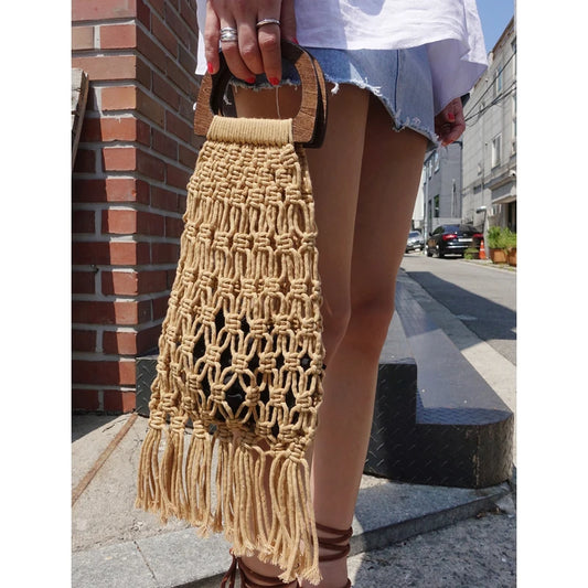 Beige macrame handbag with tassels held by a person on a city street.