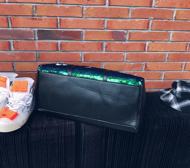 Black clutch bag with green accents on a black surface against a brick wall.