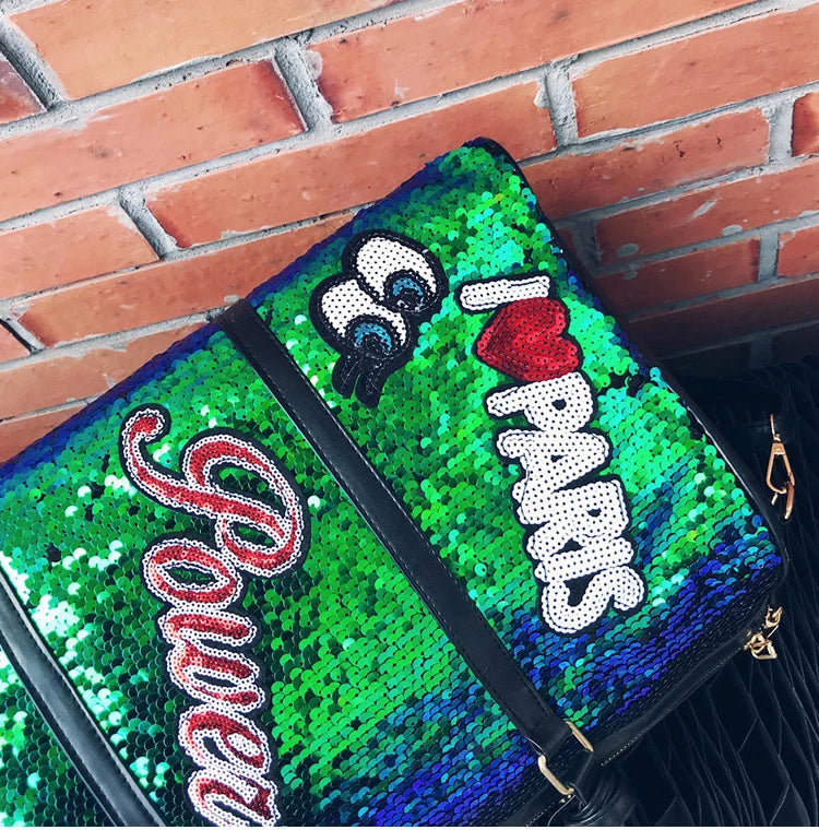 Green sequin clutch with 'I ❤️ Parks' text against a brick wall.