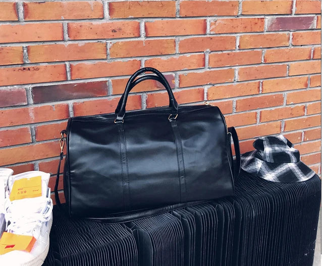Black leather duffel bag on a black bench against a brick wall.