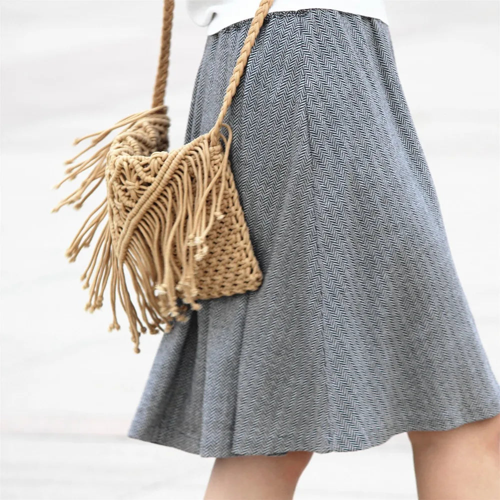Person wearing a gray skirt with a woven bag on a white background