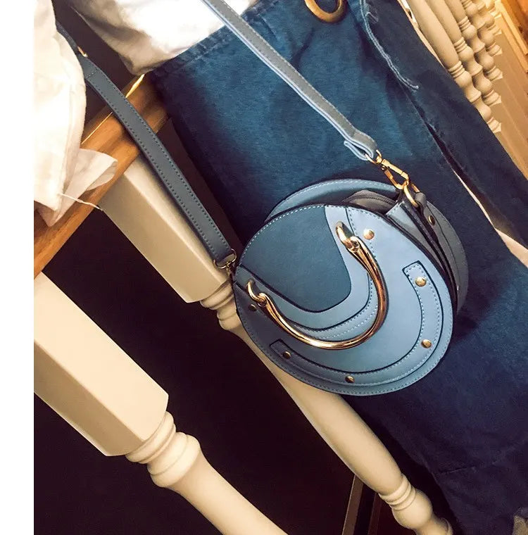 Blue handbag with gold accents on a chair. Sold at PeachyBeanz.