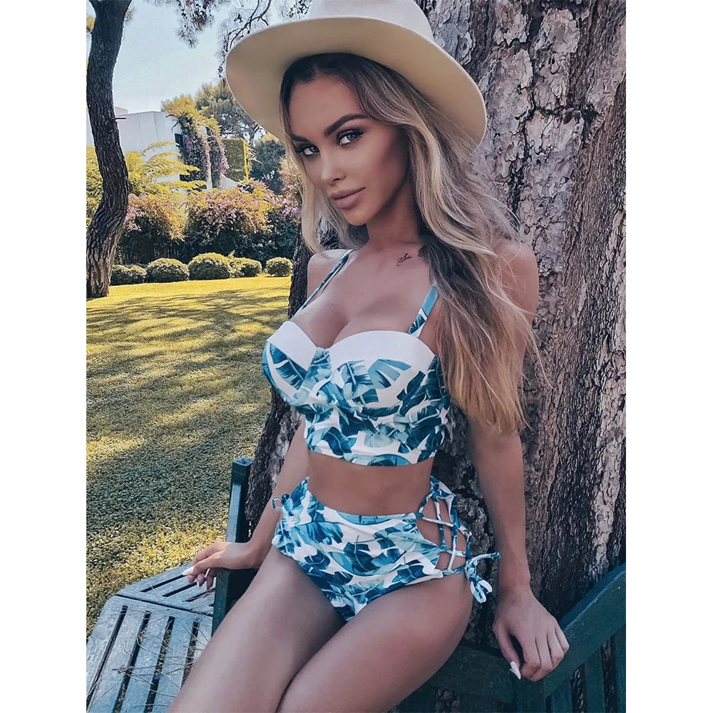 Woman in a blue and white patterned bikini sitting against a tree outdoors.