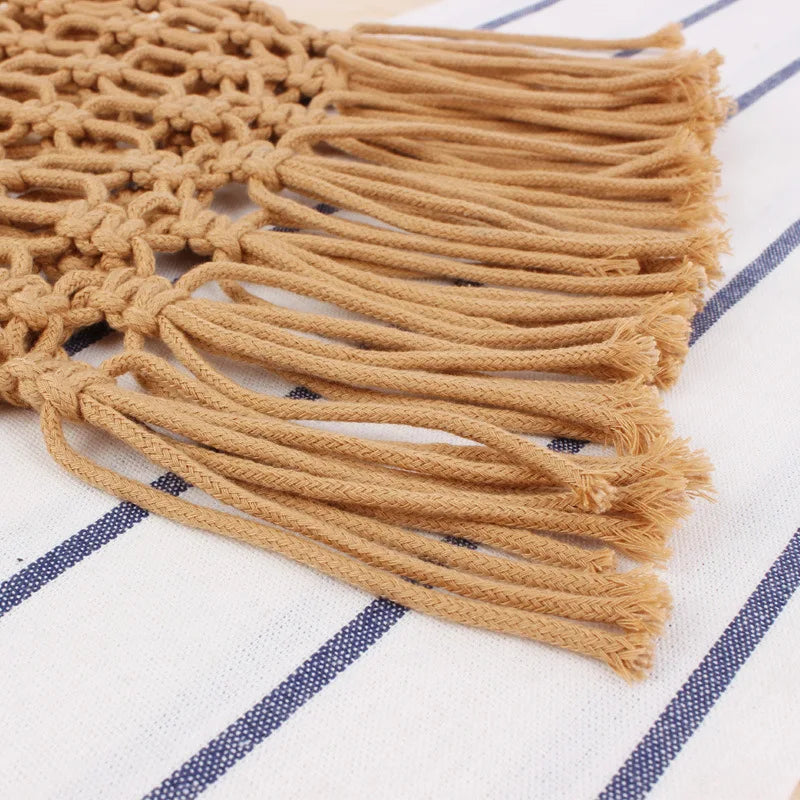 Close-up of a beige macrame wall hanging with tassels on a white and blue striped background.