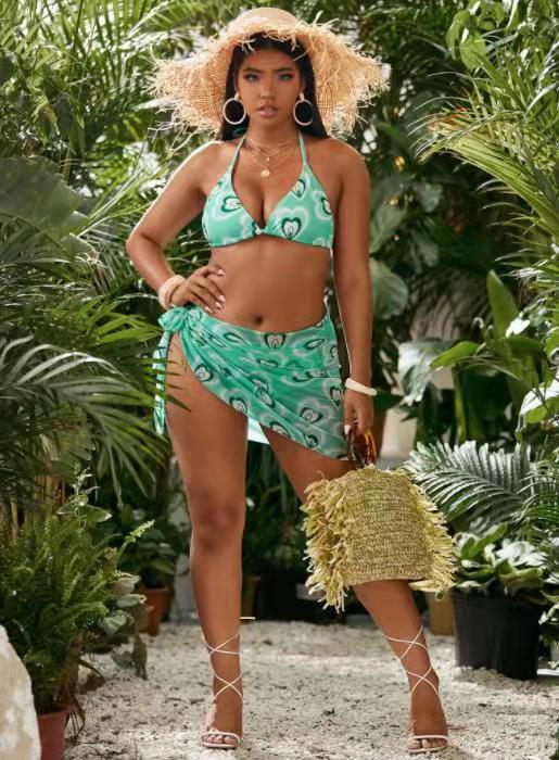 Woman in a green patterned bikini and straw hat standing among plants sold at PeachyBeanz.