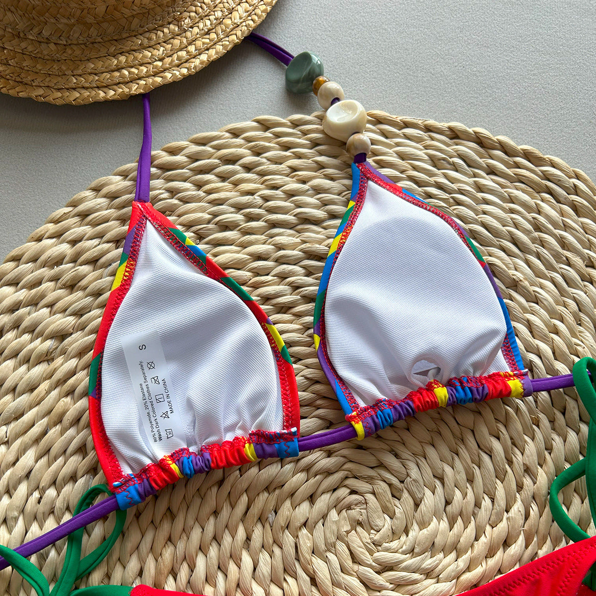 Colorful bikini top with rainbow straps on a woven mat