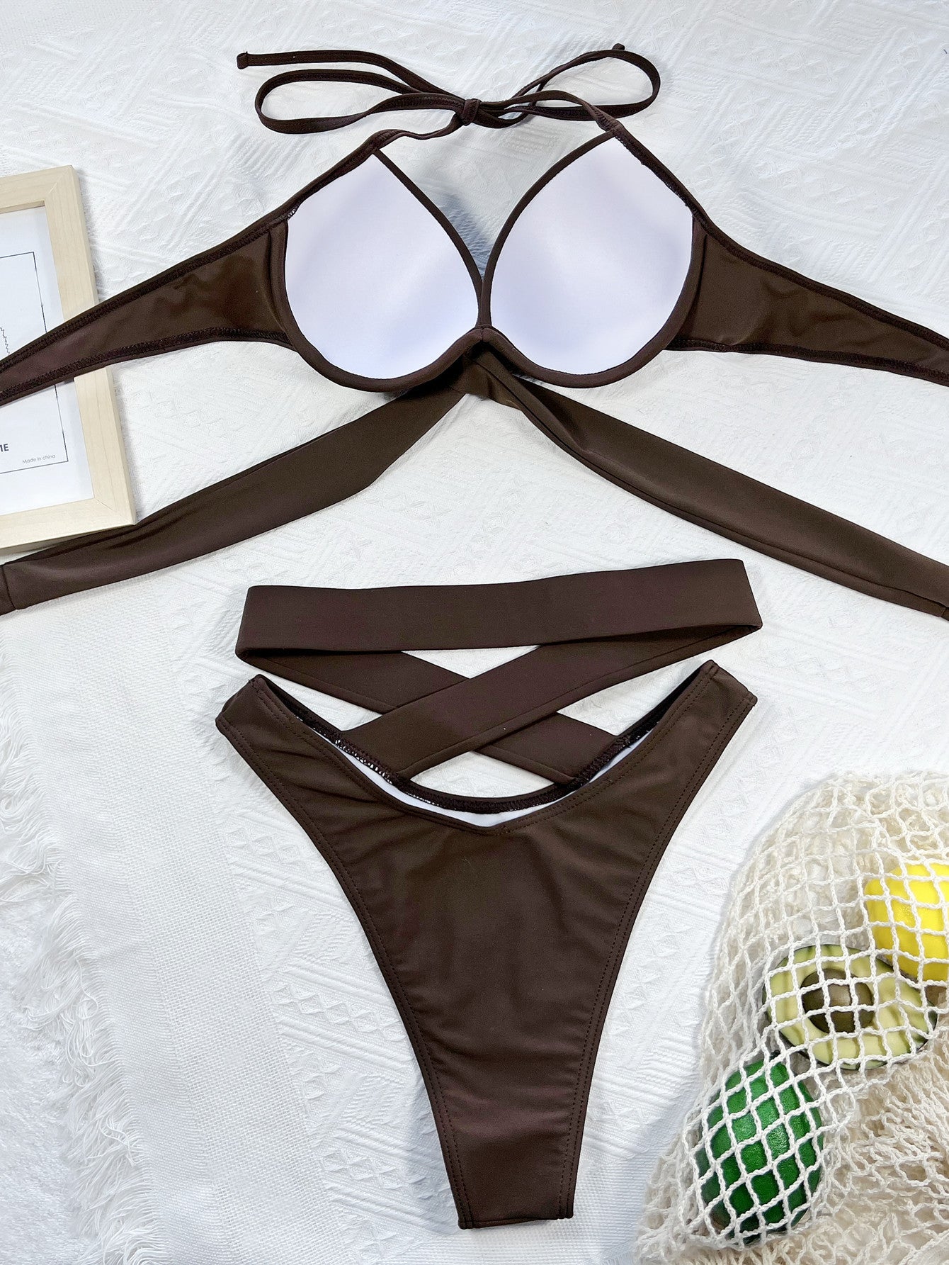 Brown bikini set on a light gray surface with a mesh bag and yellow item in the background.