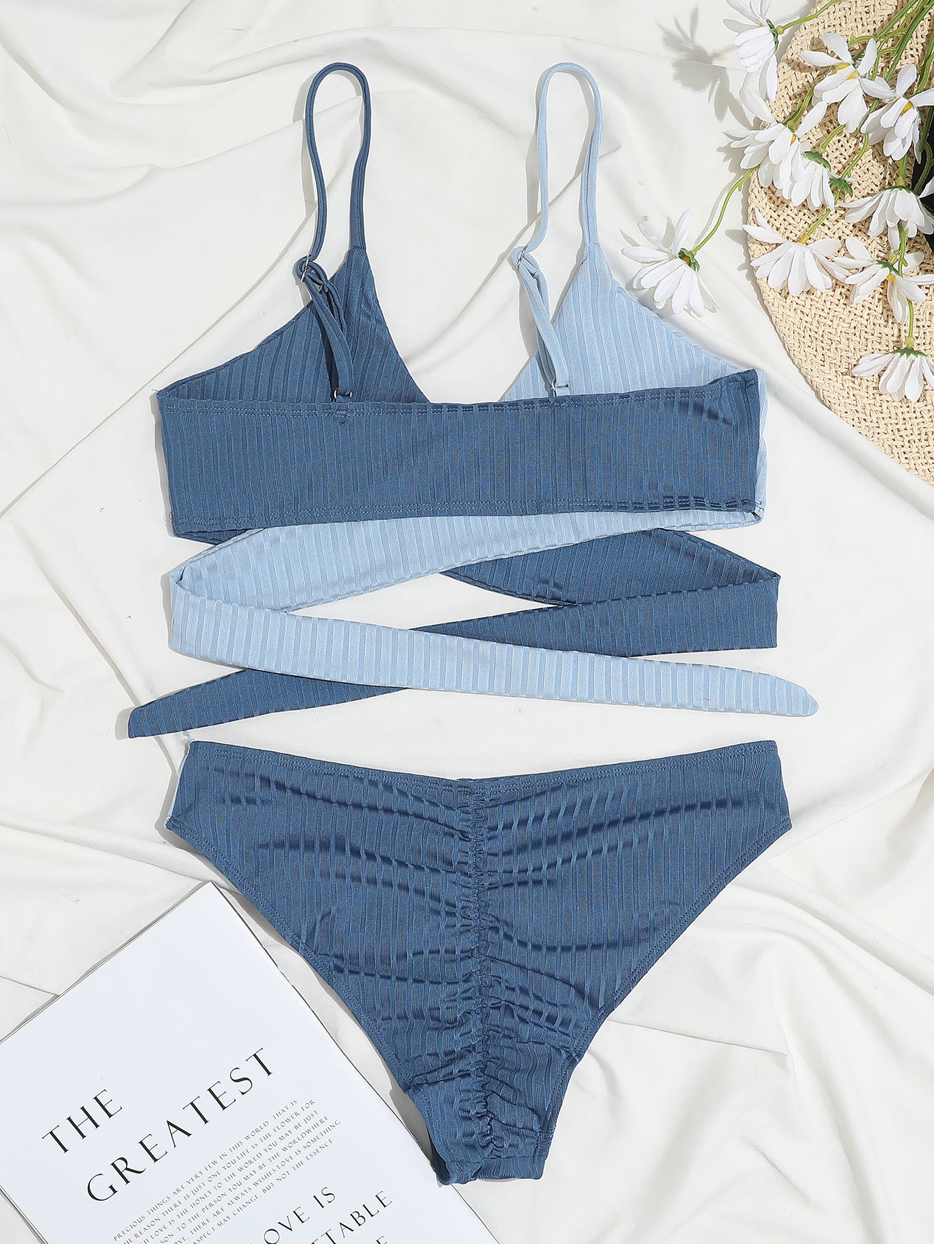 Blue bikini set on a white surface with a magazine and flowers.