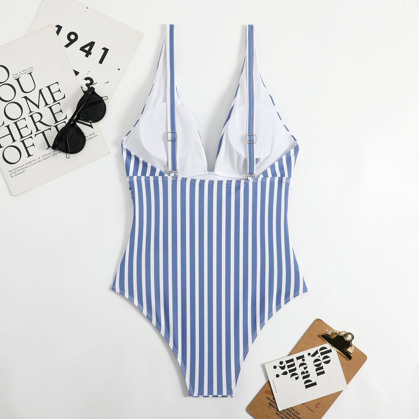 Blue and white striped swimsuit on a white surface with sunglasses and a magazine.