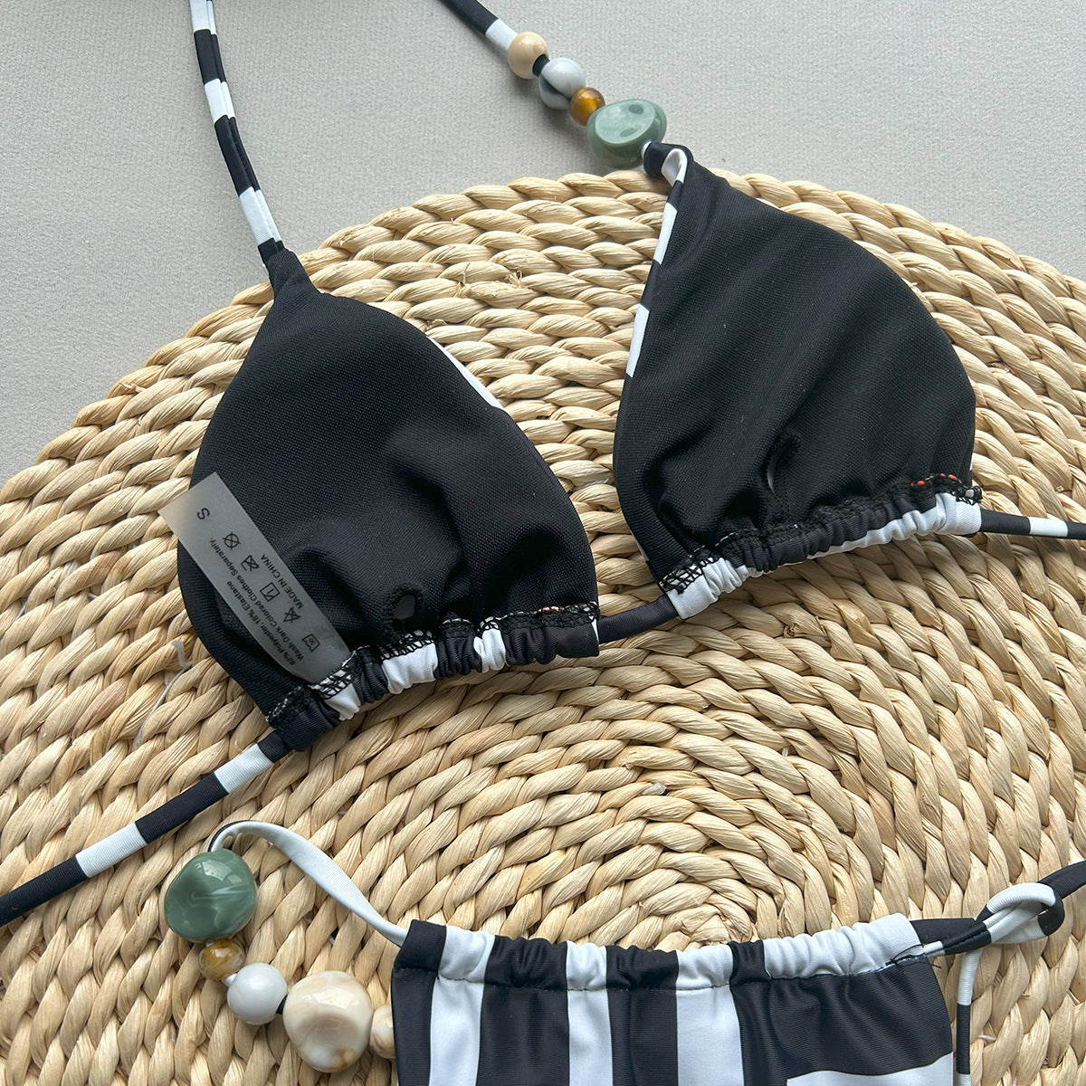Black and white bikini set on a woven mat with decorative beads.