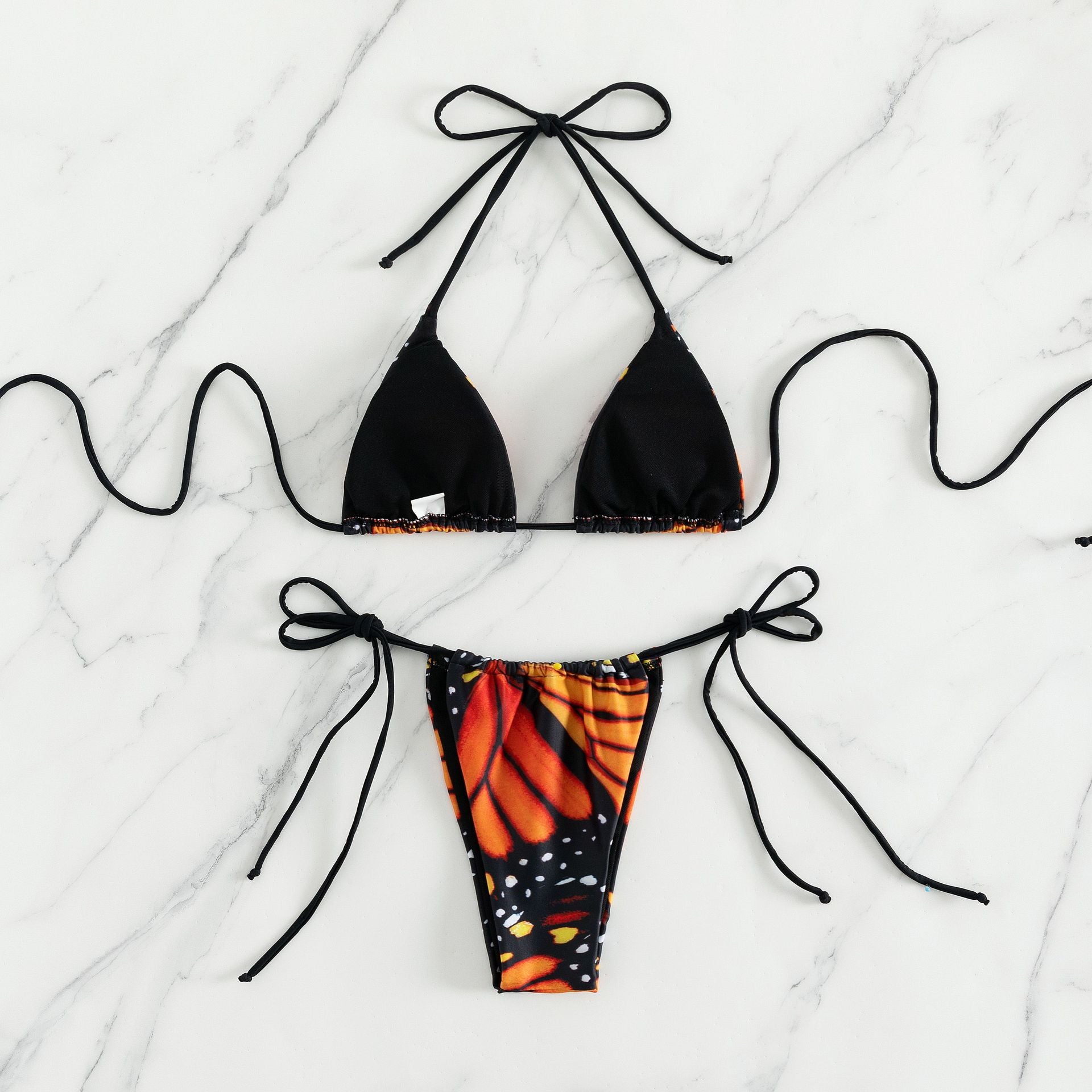 Black bikini top and butterfly-patterned bottom on a marble surface