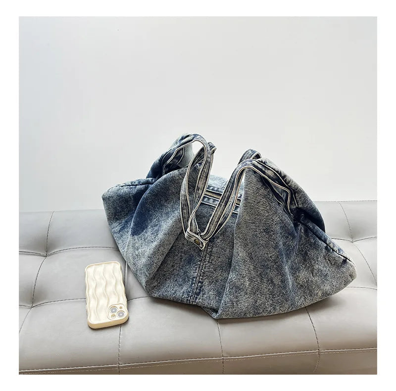 Denim bag on a light gray couch with a phone next to it