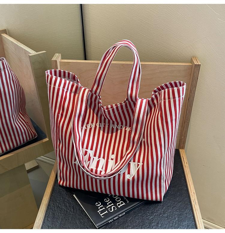 A red and white vertically striped canvas tote bag with white text reading 'stay in nature' and 'Emily' on the front, resting on a wooden chair.