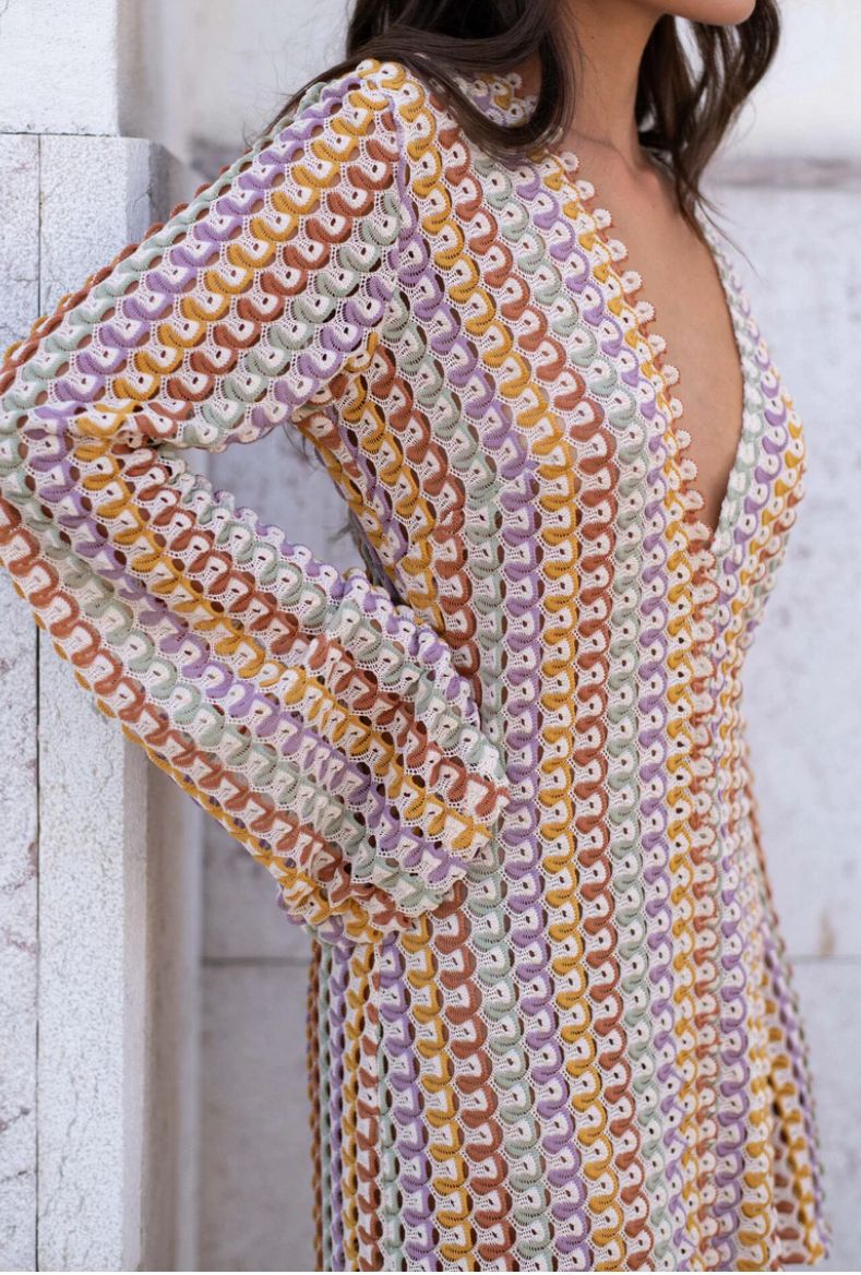 Colorful patterned dress worn by a person against a light stone wall.