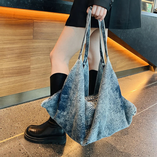 Person holding a denim bag on a sidewalk with a blurred background