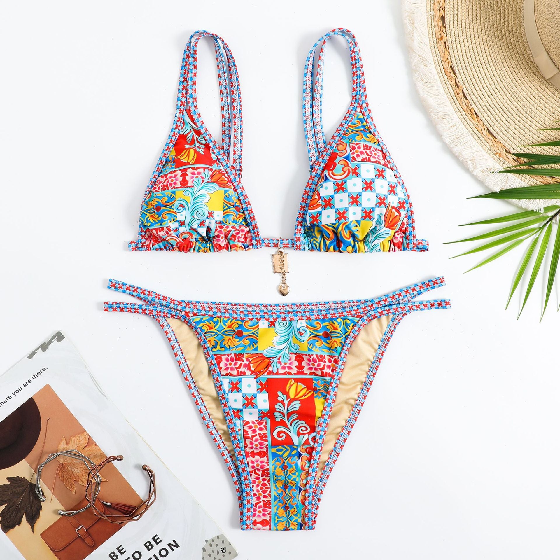 Colorful patterned bikini set with a hat and magazine on a white background